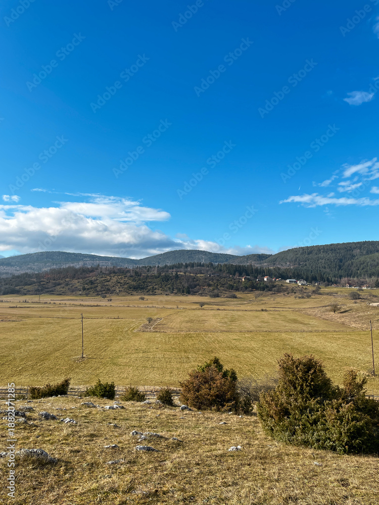 Obraz premium Wide agricultural fields stretch across a Bosnian valley with forested hills in the distance. The image conveys space, sustainability, rural economy, and natural balance.