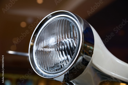 A vehicle headlight with ribbed lens and chrome ring is brightly lit indoors