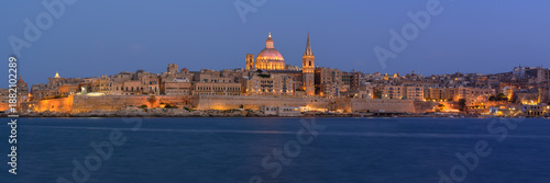 Panoramic view of Valletta Skyline at dusk seen from Sliema Harbour with lights on St. Pauls Cathedral, Malta.