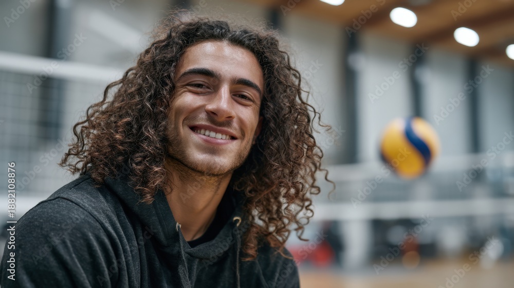 Fototapeta premium Young caucasian male smiling in gym with volleyball in background.