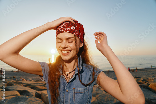 Photos smiling woman with bandana enjoying sunset on rocky beach, casual outfit, natura