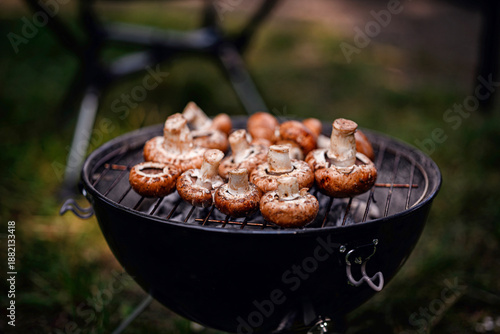 Fresh mushrooms are grilled over hot coals on a charcoal barbecue during outdoor camping or picnic.