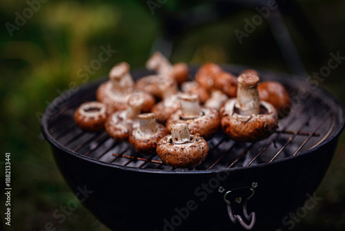 Fresh mushrooms are grilled over hot coals on a charcoal barbecue during outdoor camping or picnic.