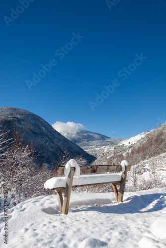 Banc en bois recouvert de neige face aux montagnes en hiver