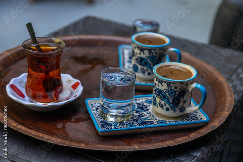 Traditional Turkish tea in a tulip glass and Turkish coffee in ornate ceramic cups served on a wooden tray with water. Authentic Mediterranean cafe culture. September, Antalya region, Turkey.
