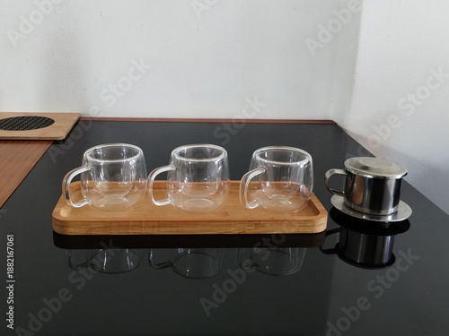 A sugar bowl next to three glass cups on a wooden stand