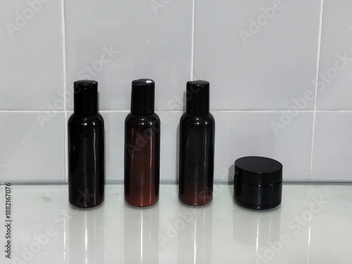 Four dark beauty product containers on a reflective surface