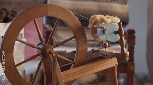 Home spinning wheel with 3d printed blue bobbin ready to use.  Wooden treadle spinning wheel with fiber and chair in the background.  Fiber arts and crafts at home with specialized tools.