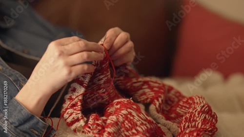 Person knitting a sweater with circular knitting needles.  Red and beige yarn being hand made into a cozy winter garment.  Close up of hands doing hobbies and crafts.