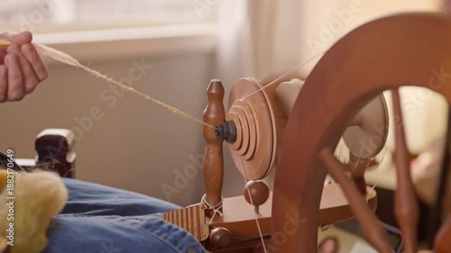 Person hand feeds raw fiber into a spinning wheel, turning wool fleece into yarn.  Close up view of large fiber turning and moving through the machine.