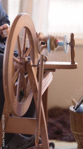 Vertical view of person spinning fiber into yarn with a traditional spinning wheel, outfitted with a 3d printed bobbin rotating on the flyer.