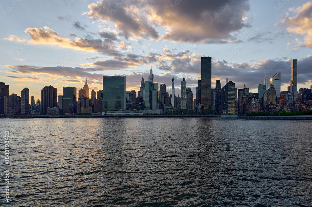 Naklejka premium Manhattan skyline at sunset over the river with skyscrapers and clouds