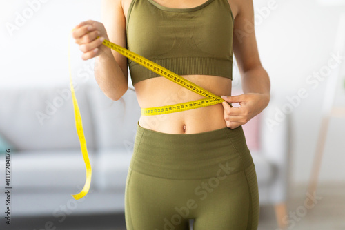 Φωτογραφία Cropped view of slim Indian woman measuring her waist with tape measure at home, closeup