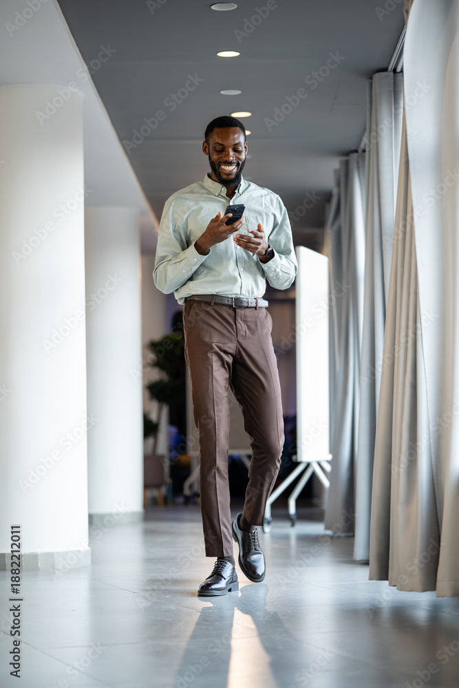 Fototapeta premium Young man walking and using smartphone in office corridor