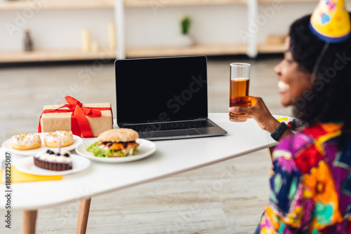 Wallpaper Mural Back-View Of African Female In Festive Hat At Laptop With Blank Screen Celebrating Birthday Or New Year Holiday Video Calling Holding Glass And Having Dinner At Home. Selective Focus, Mockup Torontodigital.ca