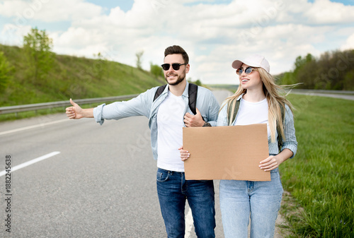 Fotografía Happy millennial couple standing along highway with empty sign, stopping car, having road trip, mockup for design