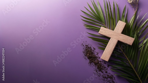 A Christian cross made of wood lies on a purple background with palm leaves and ash for Ash Wednesday.