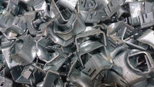 Metal industrial brackets stacked in bulk showing raw texture, manufacturing detail, silver surface, repetition, pattern, and metallic tones.