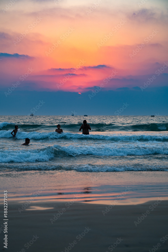 Fototapeta premium Sunset at Colva Goa beach in South India, silhouette of people swimming in Arabian Sea, tropical west coast, Asia, vacation destination