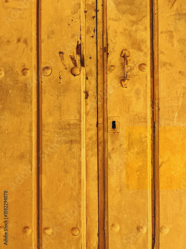 Old decayed yellow steel door with handle and keyhole.