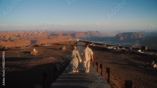 Couple is traveling in Saudi Arabia, AlUla. Man and woman walk away with the view of canyon and sand rocks of Al Ula.