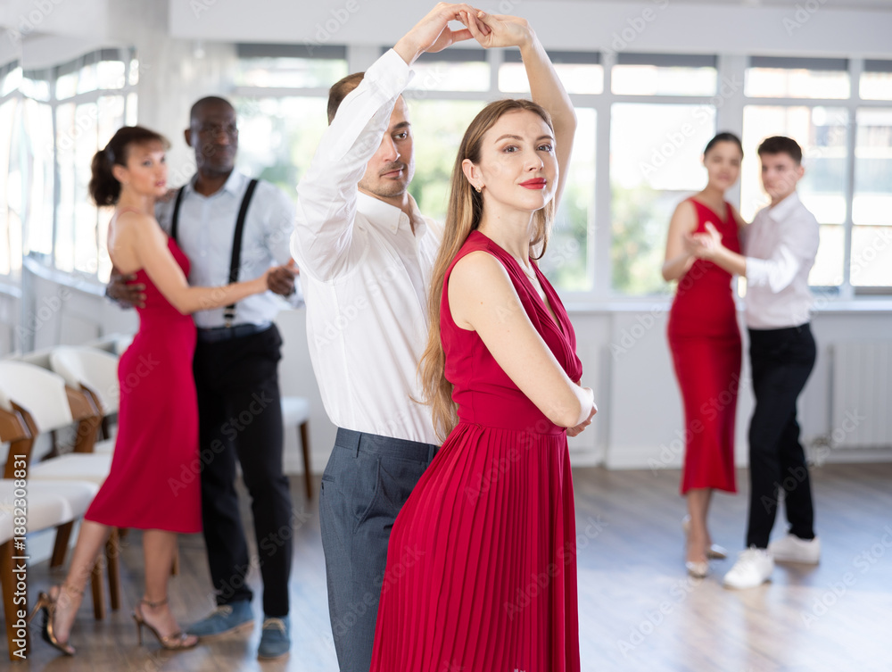 Obraz premium Expressive young adult woman in elegant vibrant red dress dancing passionate bachata with male partner during group dance class for adults