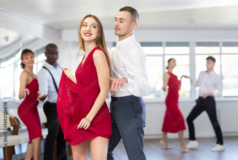 Obraz premium Group of young contemporary active people practicing vogue dancing movements while training twist or charleston in dance hall