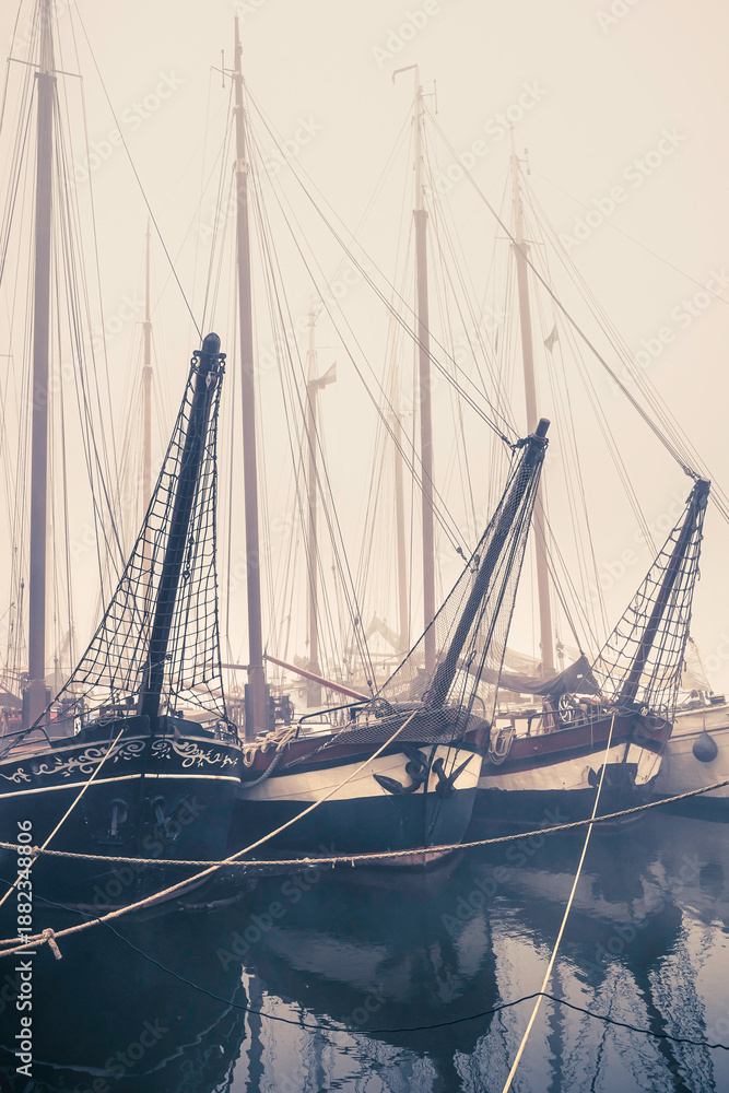 Obraz premium Historic cargo boats resting quietly on the river quay in Kampen during a foggy autumn morning