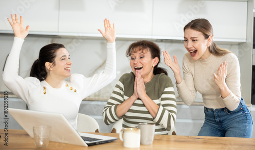 Φωτογραφία Female friends are sitting at table, reading letter on computer about invitation to study and scholarship, rejoicing at good news, are glad over victory