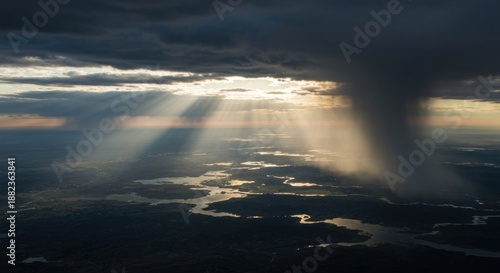 Aerial view of a landscape illuminated by sunbeams breaking through a dark, stormy sky