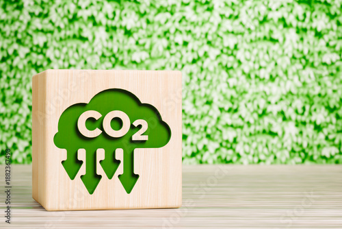Wooden block with CO2 cloud icon and arrows on green leaves background carbon footprint concept