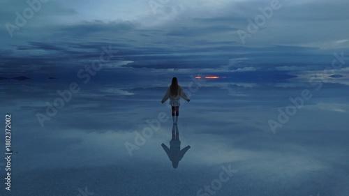 A solitary figure standing on the reflective surface of Bolivia's Salar de Uyuni during a tranquil late afternoon
