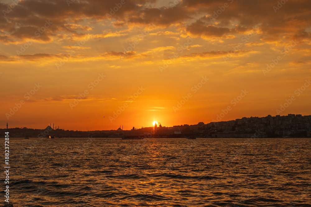 Naklejka premium Beautiful glowing sunset on the European side of Istanbul, Turkey from Bosphorus toward Karakoy and Eminonu, with the silhouettes of Galata Tower and Suleymaniye Mosque against burning sky