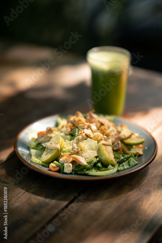 Tazón de ensalada fresca verde con pollo y jugo verde sobre una mesadme madera bajo los rayos de sol,  comida saludable