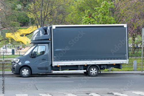 Gray delivery truck mockup parked on the roadside with a large cargo area, surrounded by greenery and a playground visible in the background during daylight hours