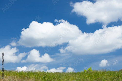 Bright blue sky with fluffy white clouds above a grassy field, showcasing a serene natural landscape ideal for outdoor themes and nature-related projects