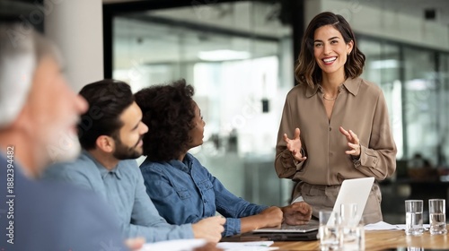 Confident female leader smiling and gesturing while leading a business meeting with a diverse team in a modern office setting.