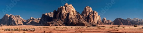 Wallpaper Mural A sweeping panorama showcasing arid terrain. Towering rock formations dominate the center, set against a deep blue sky. The foreground is sandy desert Torontodigital.ca
