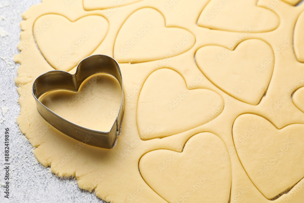 Obraz premium Heart shaped cookie cutter and raw dough on table, closeup