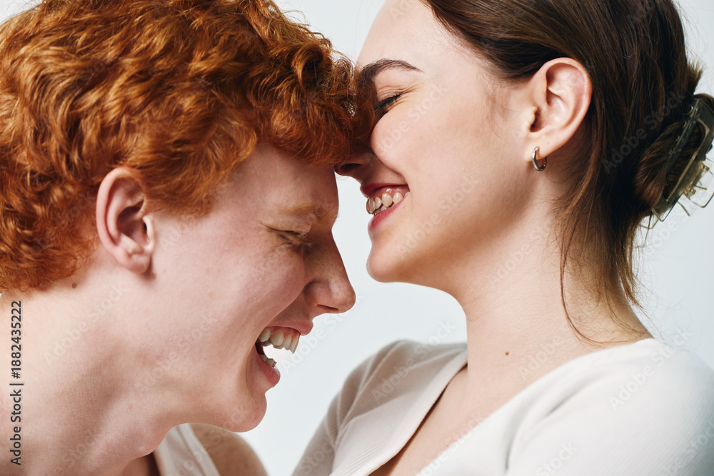 Naklejka premium Young couple with close faces laughing and enjoying tender moment, smiling woman and man with red hair in casual clothes on white background expressing happiness and love.