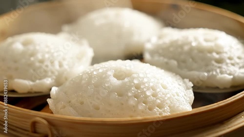 Delicious and fluffy white steamed rice cakes possibly Idli or Appam beautifully arranged in a traditional bamboo steamer basket showcasing authentic Asian or Indian breakfast cuisine with a soft inv.