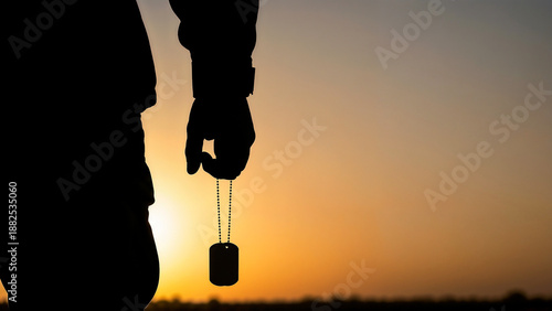 Soldier’s hand holding dog tag at sunset symbolizing remembrance and identity