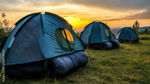 Two portable emergency shelters set up on a grassy hill at sunset with golden light illuminating the sky