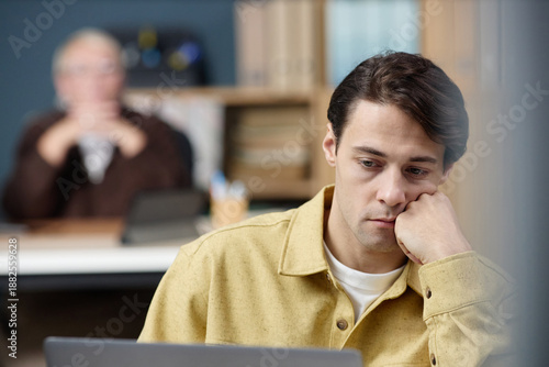 Konstfotografi Young adult Caucasian man sitting at desk resting chin on hand, appearing though