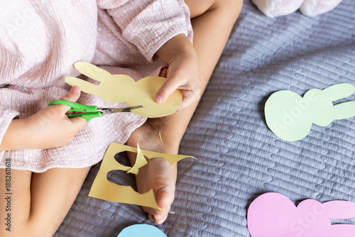 Young child cutting bunny shapes out of colored paper on a bed