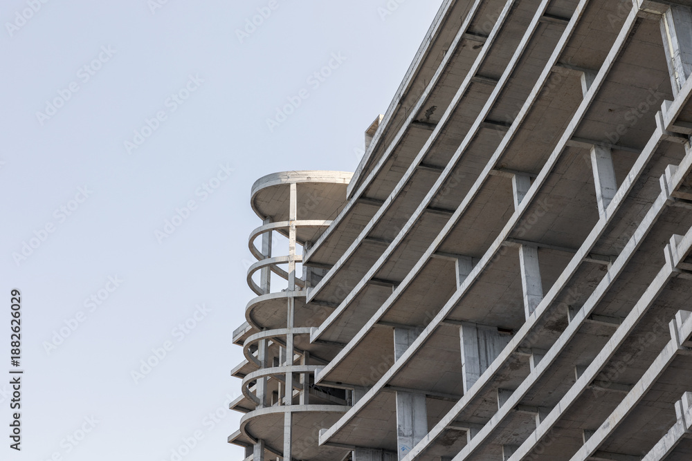 Naklejka premium A concrete building under construction rises with circular ramp columns