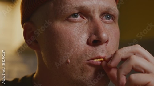 Close-up frontal shot of a man chewing a potato chip. Focus on facial expression and mouth, shallow depth of field, warm indoor kitchen lighting in the background. High quality 4k footage