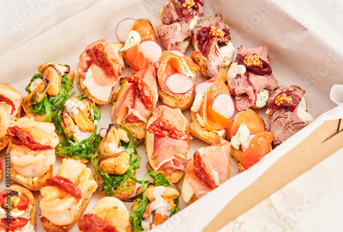 A variety of appetizers are neatly arranged on a platter. The selection includes seafood, different meats, and fresh vegetables. This spread is suitable for a gathering or event