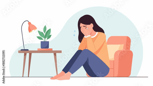 A person sits on the floor, crying into their hands next to a chair and table