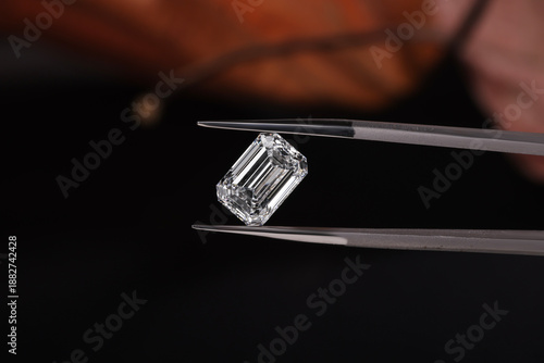 Slika na platnu Close-up of an Emerald cut diamond held with precision tweezers against a dark background, showcasing clarity, brilliance, and luxury gemstone evaluation
